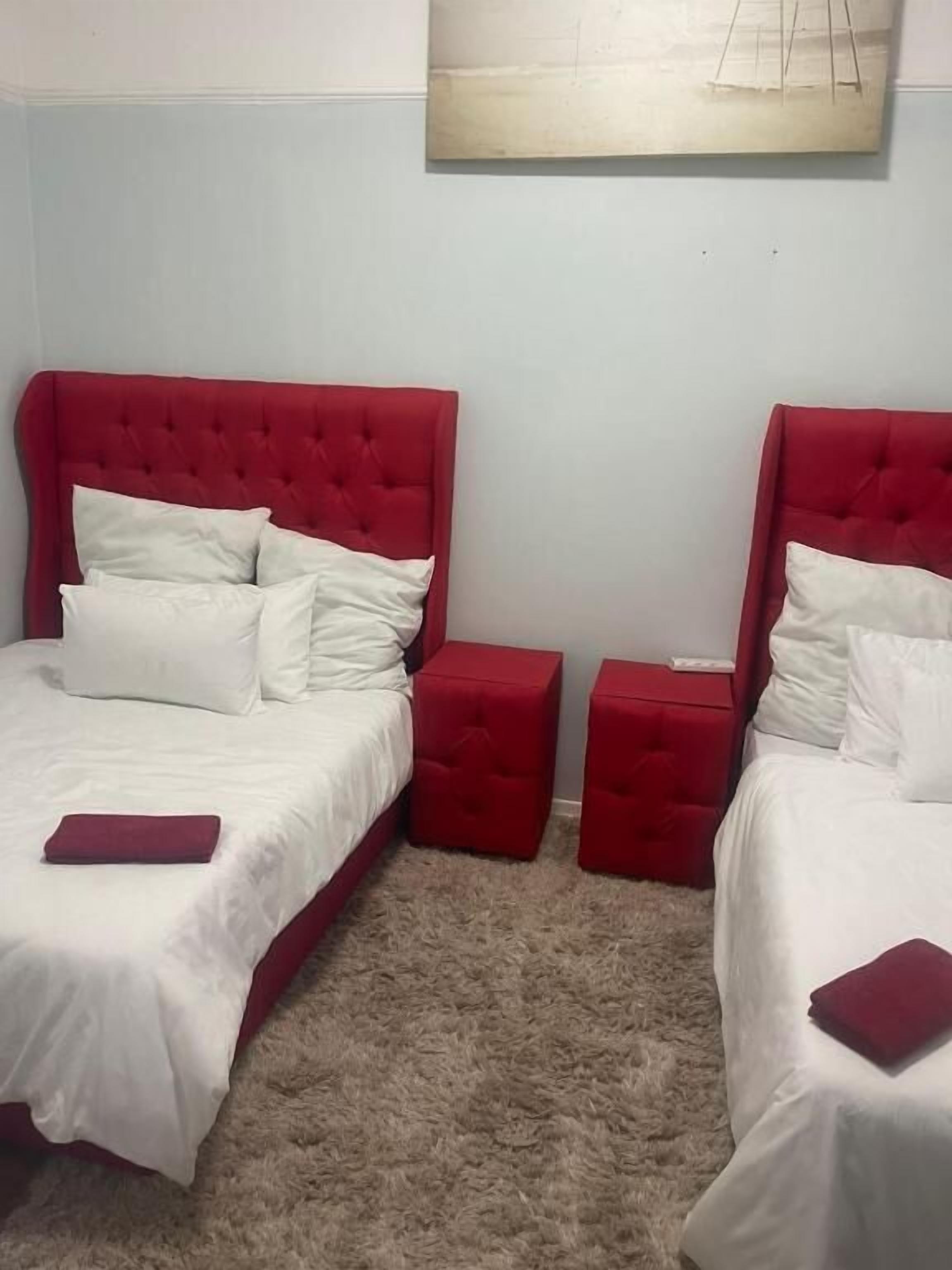 Un dormitorio con dos camas, cada una con cabecero rojo, ropa de cama blanca y una almohada roja sobre la cama. Hay dos mesitas de noche rojas entre las camas.
