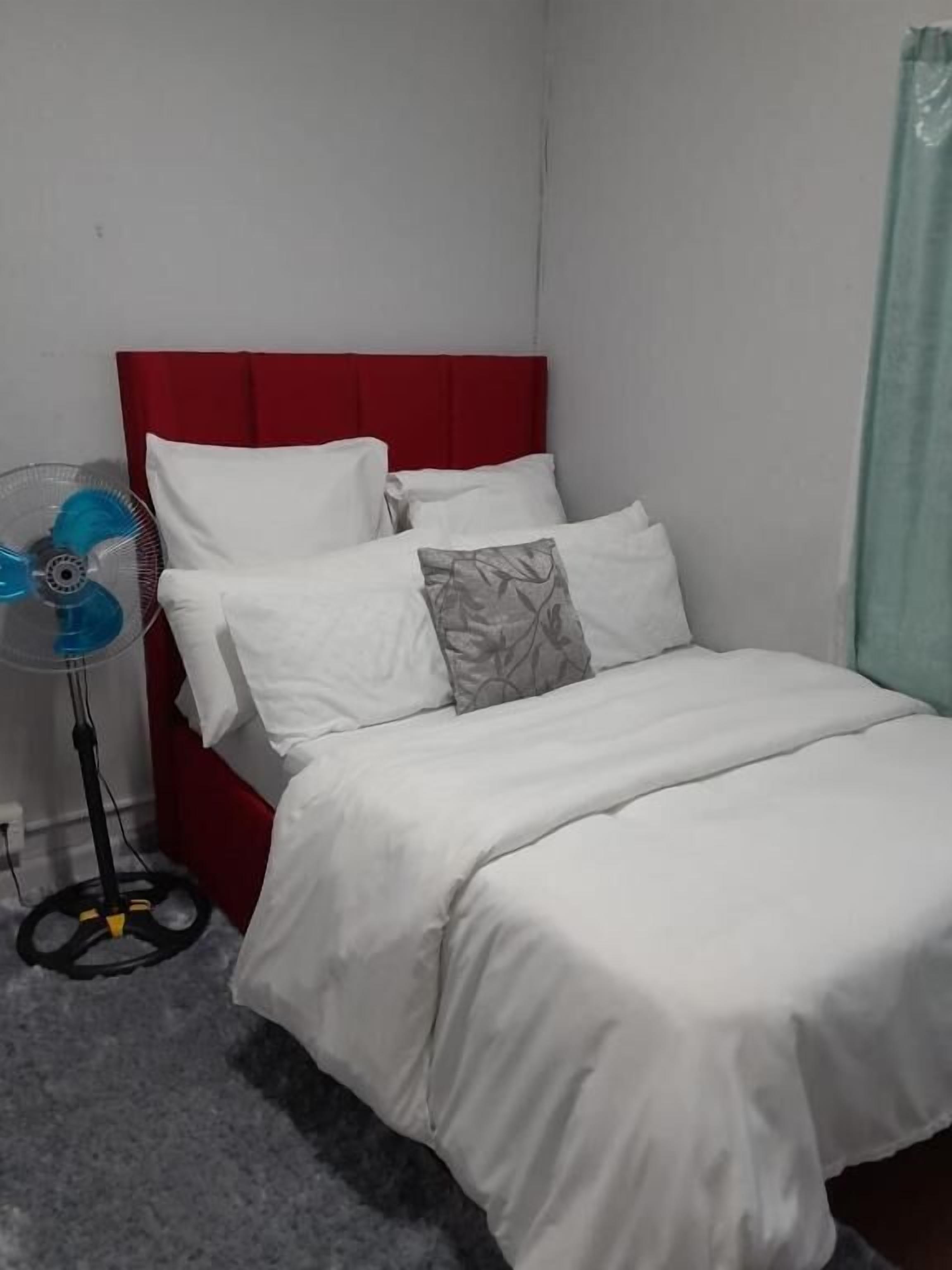 A bed with white bedding, a red headboard, and a standing fan.