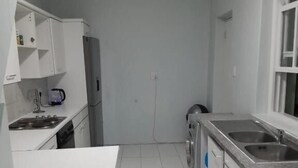 Una cocina compacta con armarios blancos, horno empotrado, lavadora y un lavamanos.
