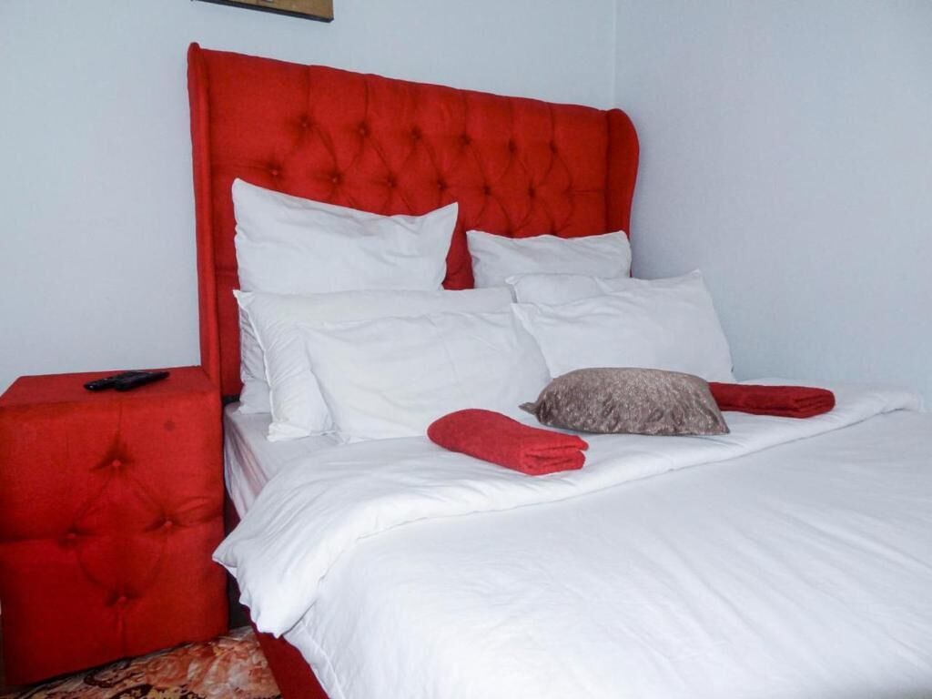 A bed with a red headboard, white bedding, and a remote control on the side table.