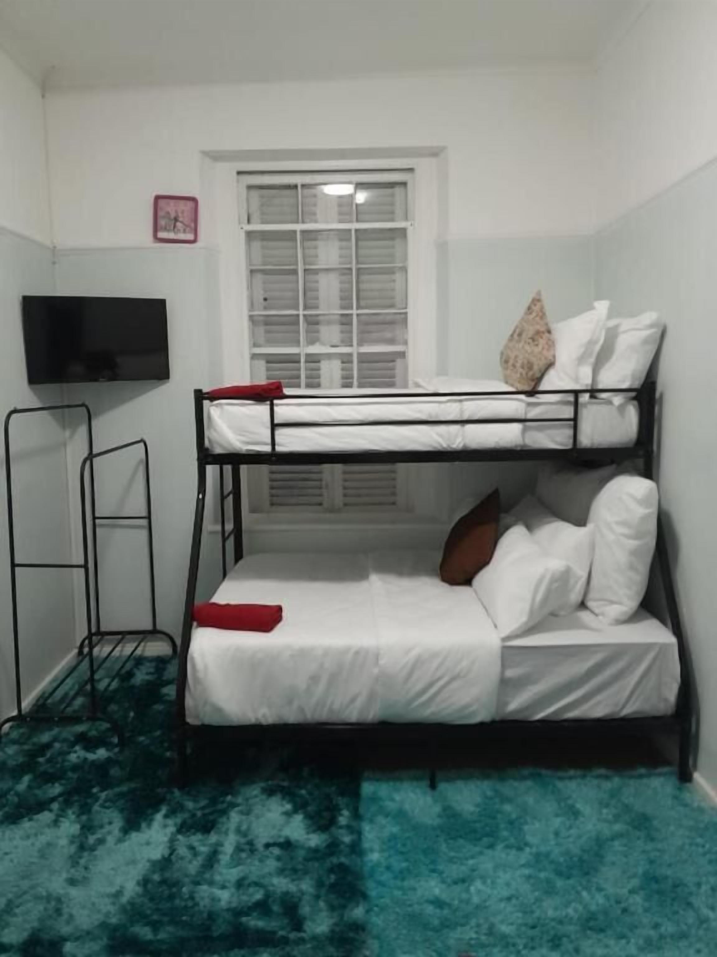 Een stapelbed met witte lakens, een rood kussen en een televisie aan de muur.