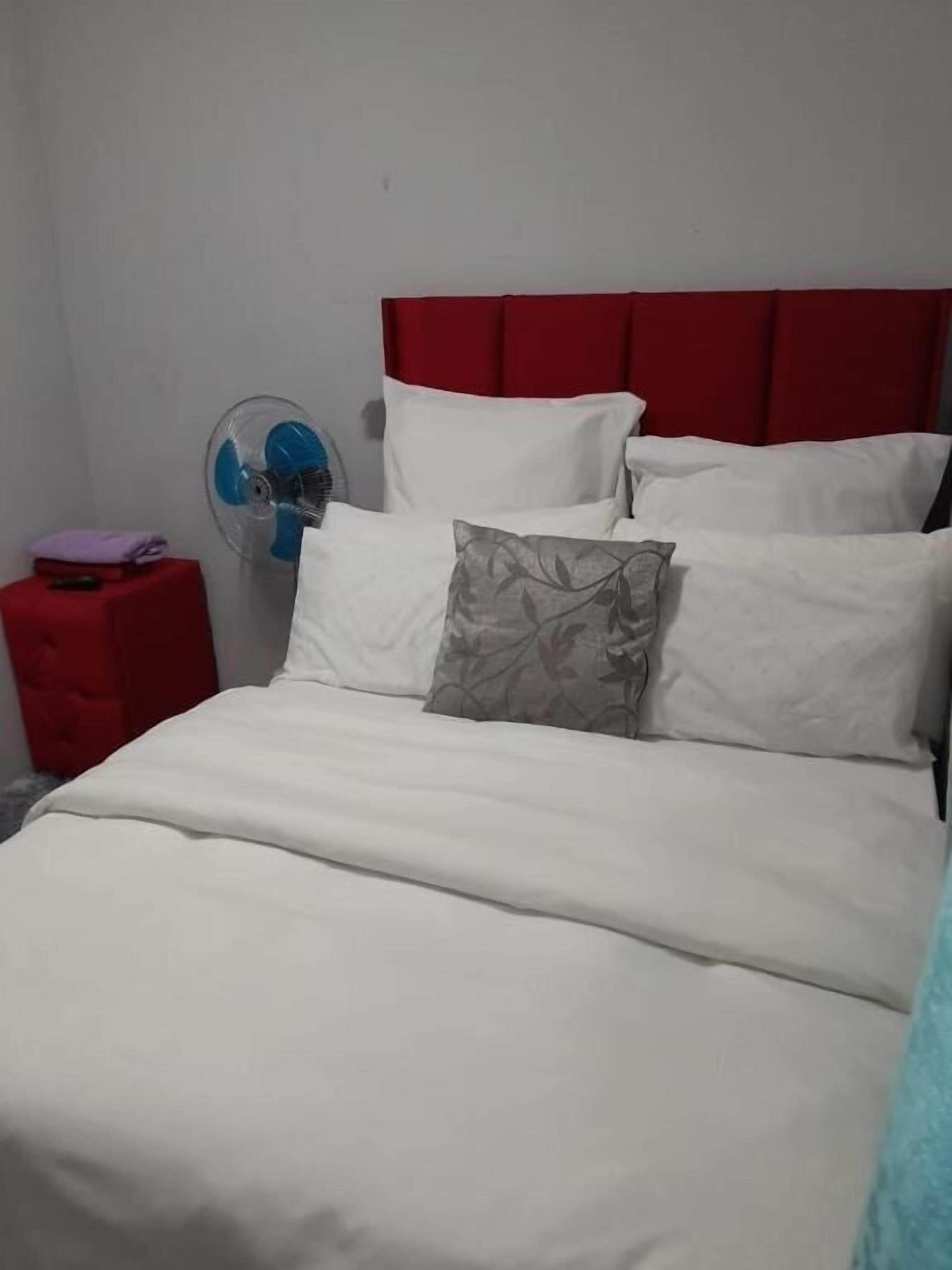 A bed with white bedding, a red headboard, and a grey pillow.