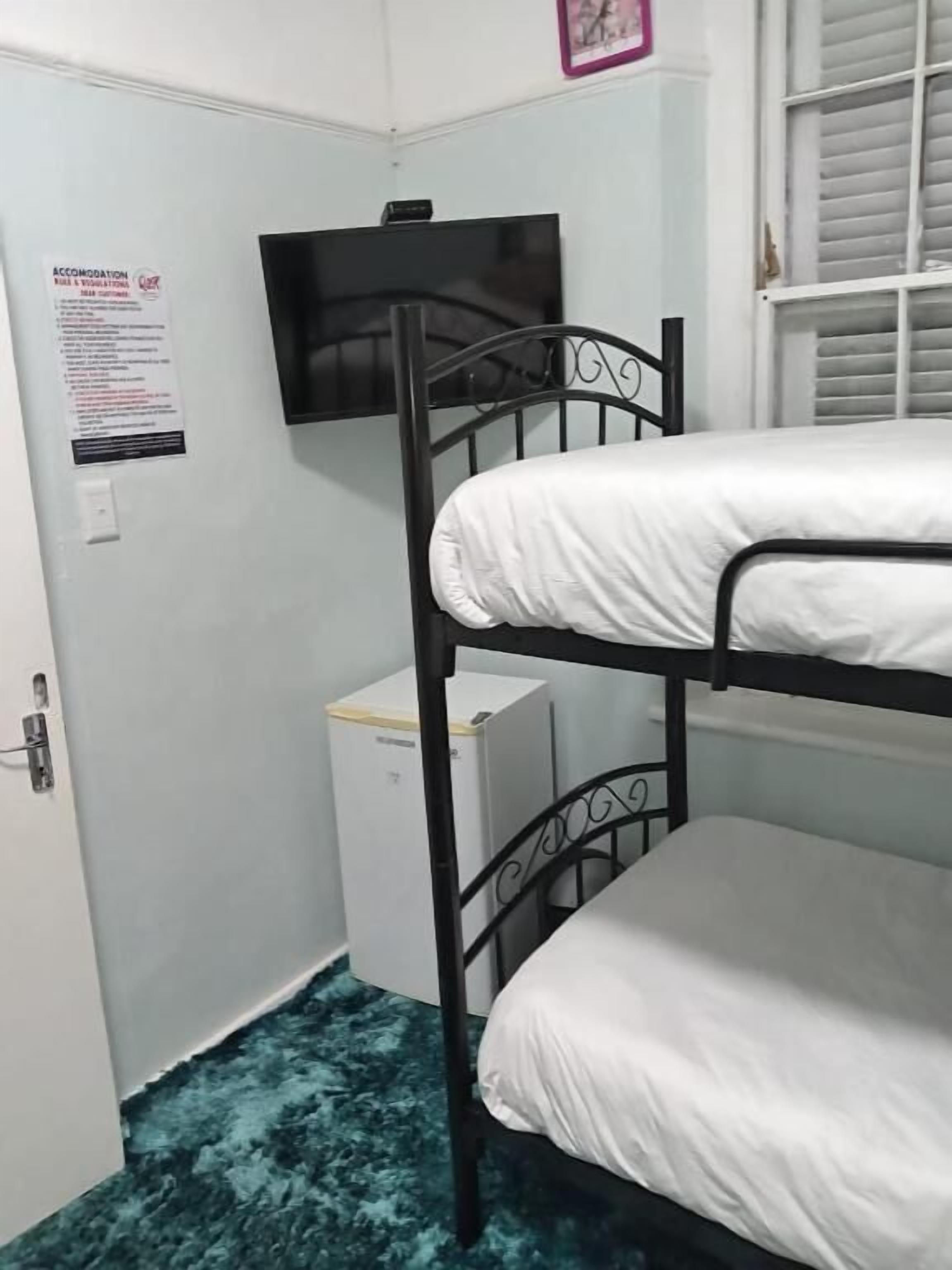 A bunk bed room with a television on the wall, a small white cabinet, and a door with a sign.