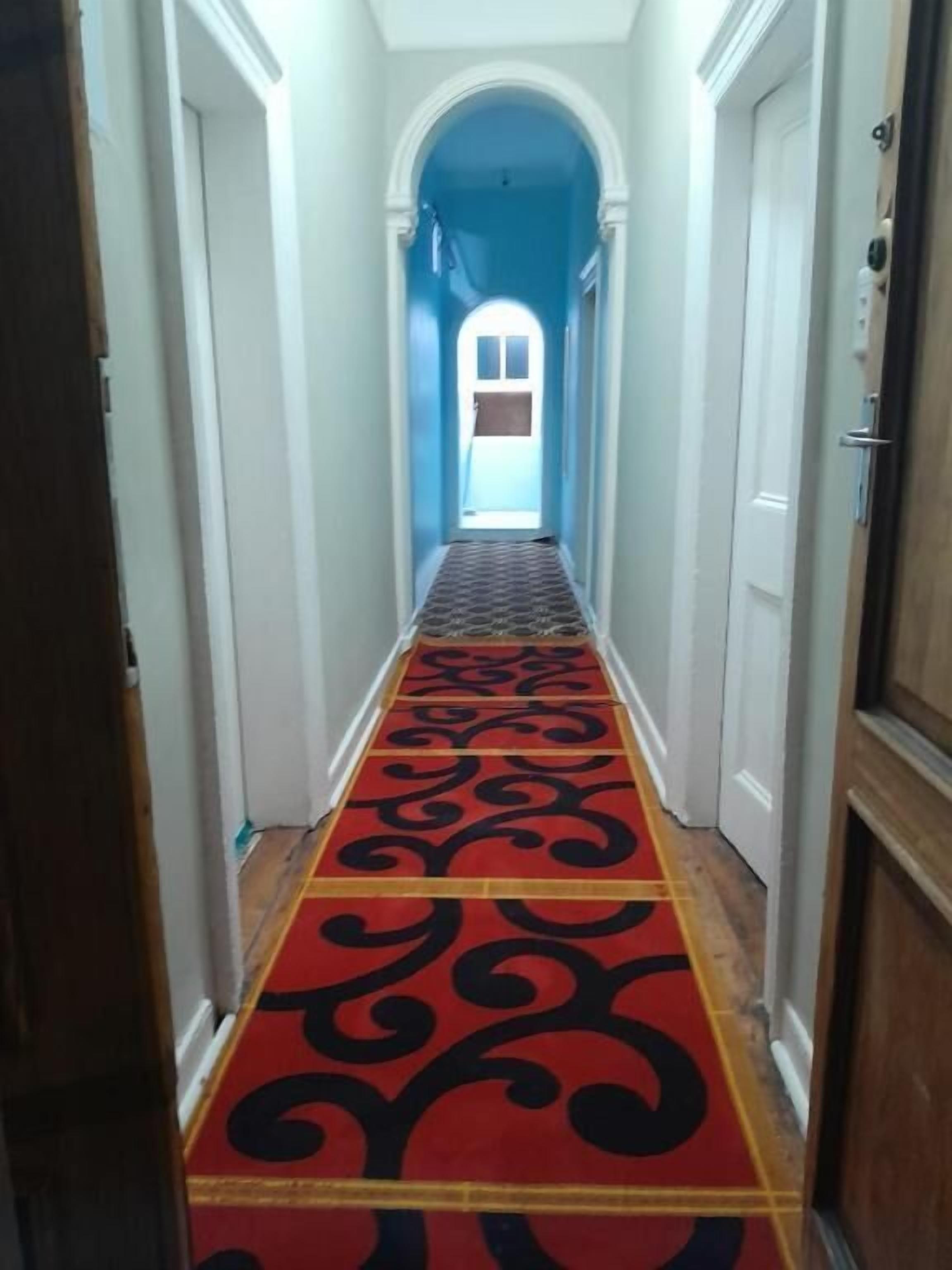 A hallway with a red carpet, white walls, and a wooden door on the right.