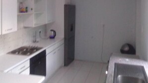 Una cocina compacta con armarios blancos, un lavamanos y una tetera.