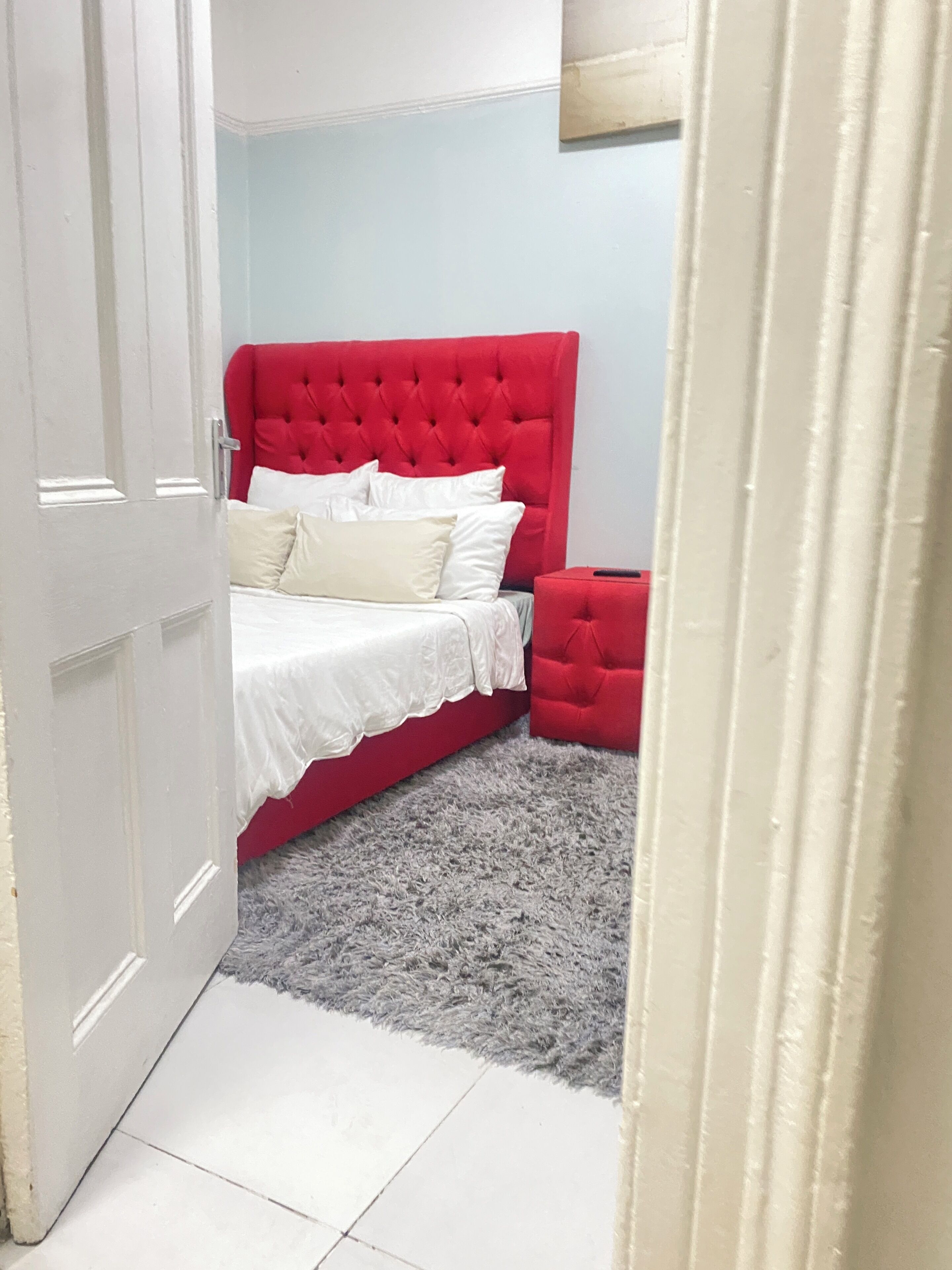 A bedroom with a red upholstered headboard, a white bedspread, and a grey shaggy rug.