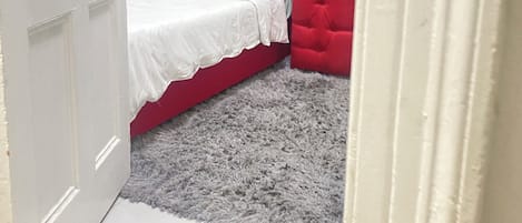 Un dormitorio con un cabecero tapizado en rojo, una colcha blanca y una alfombra mullida de color gris.