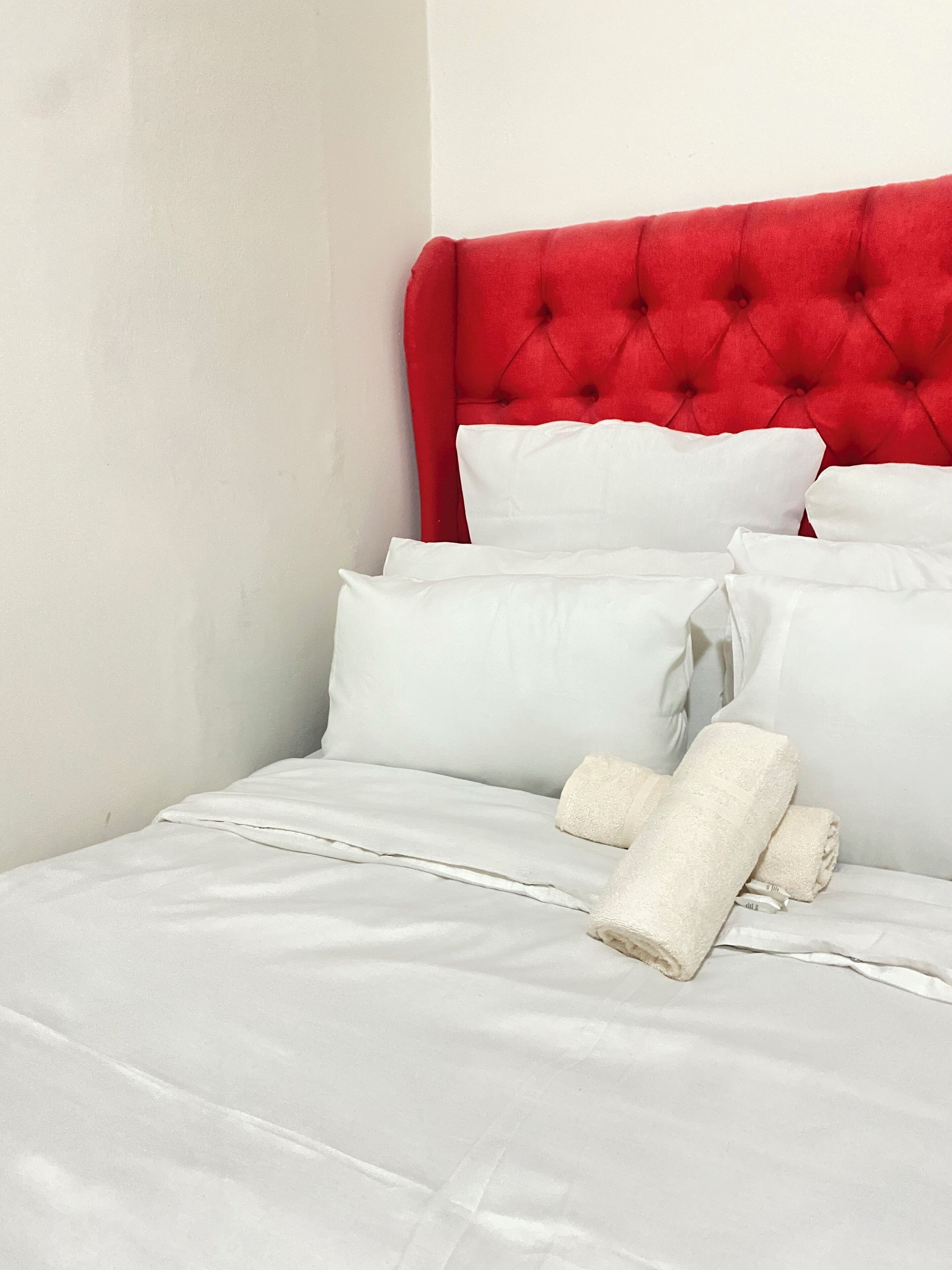 Una cama con ropa de cama blanca y un cabecero rojo.