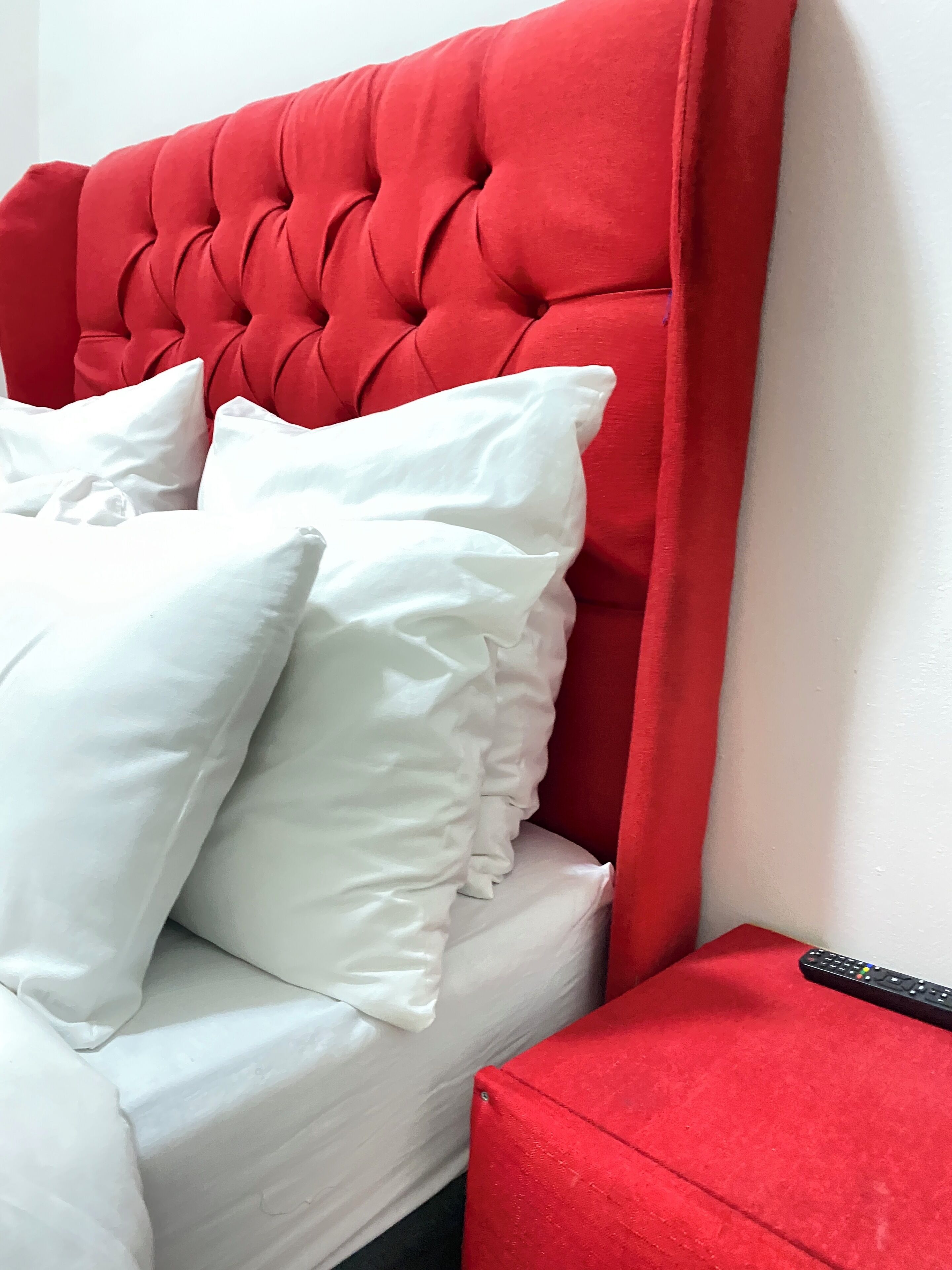 A bed with a tufted headboard, white pillows, and a red accent piece.