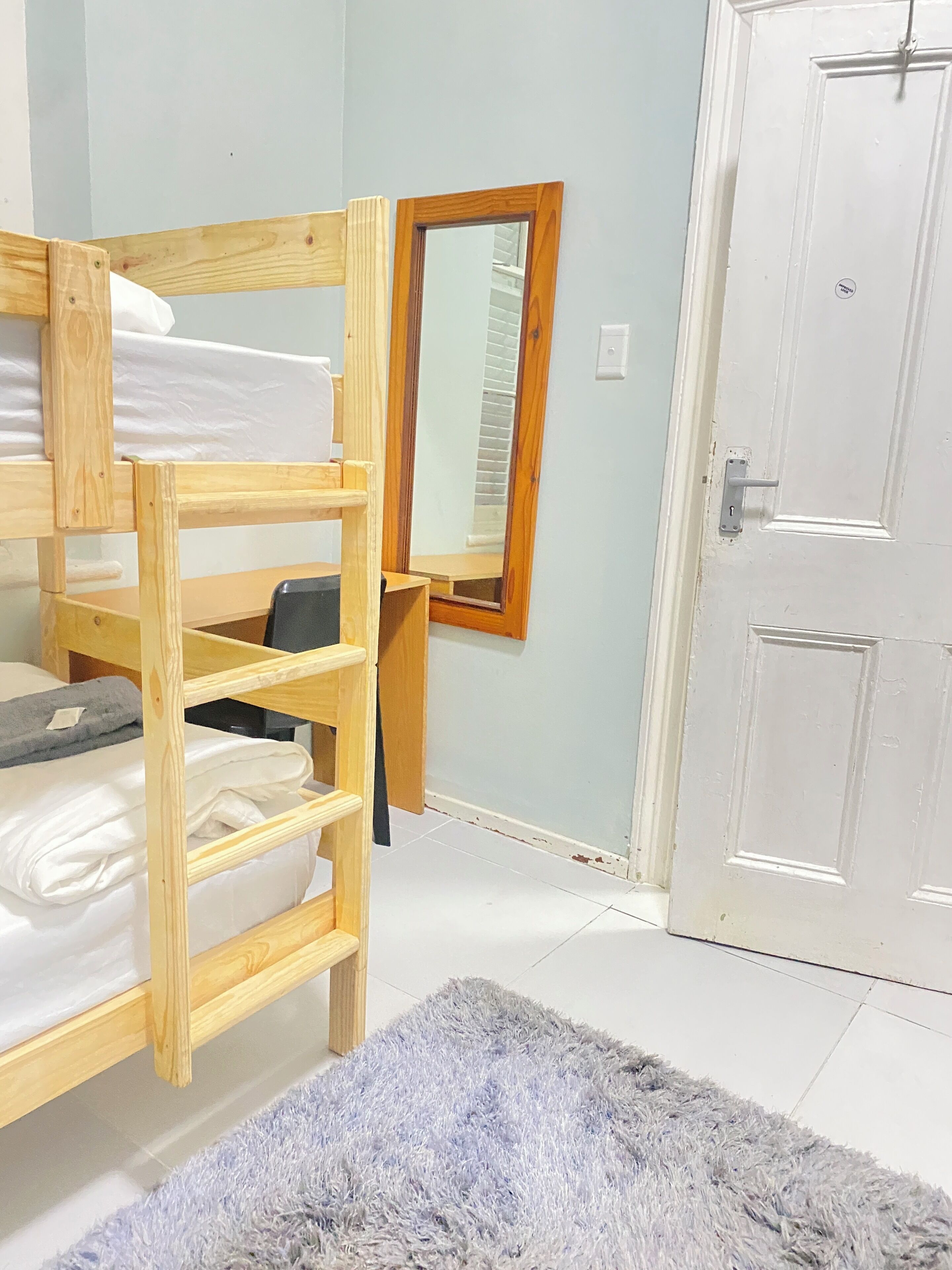 Ein Etagenbett mit Holzrahmen, ein Spiegel, eine weiße Tür und ein grauer Teppich.