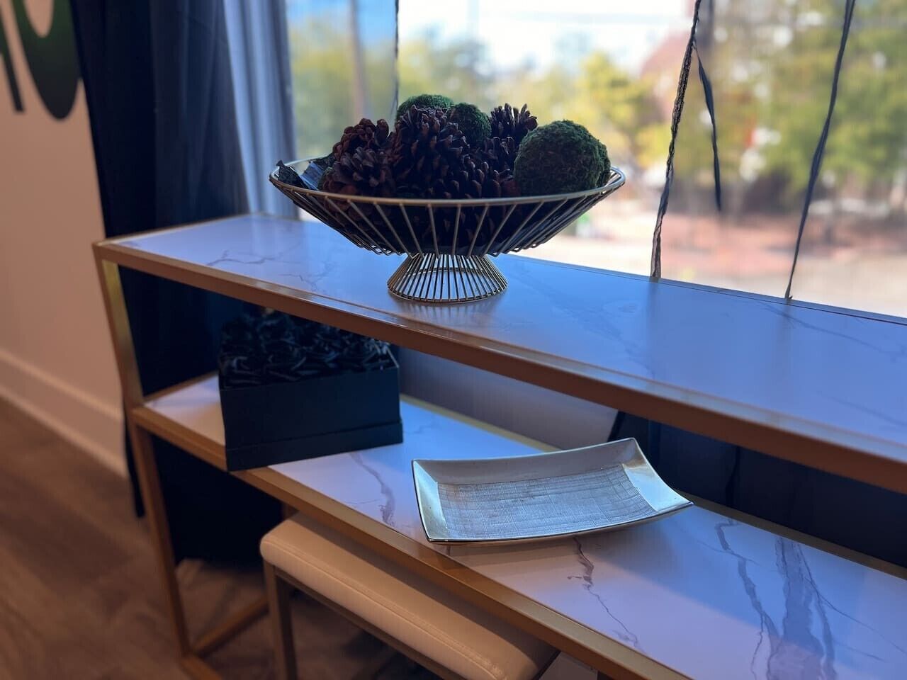 Puinen pöytä, jonka päällä on metallinen kulho, jossa on käpyjä ja sammalpalloja, musta laatikko ja valkoinen lautanen, jossa on ruokalista.