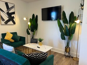 Uma sala de estar moderna com um sofá, uma mesa de centro, uma televisão e plantas verdes grandes.