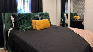 Quarto com cama, espelho, mesinha e janela com cortinas.
