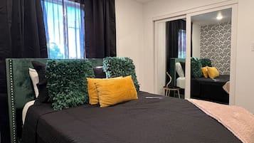 Un dormitorio con cama, espejo, una mesita y ventana con cortinas.