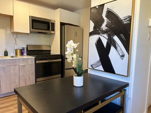 A modern kitchen with stainless steel appliances, a dark wooden table, and a white vase with flowers. - Fair Park Area | Free Parking | Slps 4 (Dallas)