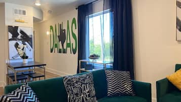 Una sala de estar con un sofá verde, una mesa de centro, un televisor y un amplio ventanal con cortinas.