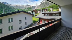 En balkong med utsikt över ett bergigt landskap, en vit byggnad och en träkonstruktion.