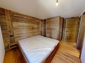 Ein Schlafzimmer mit Holz-Kopfteil, einem Bett, einer eingebauten Ablage und einem Kleiderschrank.
