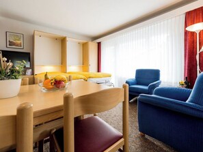 A hotel room with a wooden dining table, a fruit bowl, a blue armchair, and a sofa. - Aiglon Appartement/Fewo 2-Bettwohnung Nr. 1 by Interhome (Saas-Fee)