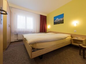 A hotel room with a bed, a window with curtains, a painting on the wall, and a bedside table. - Aiglon Appartement/Fewo 2-Bettwohnung Nr. 1 by Interhome (Saas-Fee)