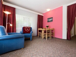 A room with a blue sofa, a red chair with a logo, a wooden table with chairs, and a pink wall with a picture. - Aiglon Appartement/Fewo 2-Bettwohnung Nr. 1 by Interhome (Saas-Fee)