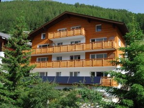 Un immeuble en bois à plusieurs étages, doté de balcons, entouré d’arbres et avec une chaîne de montagnes en arrière-plan.