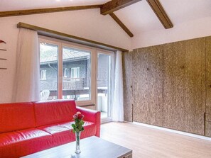 A room with a red sofa, a white table, and a large window with a view of a house. - Alouette Appartement/Fewo 6-Bettwohnung Nr. 18 by Interhome (Saas-Fee)