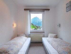 A small, simple room with two single beds, a window with a mountain view, and a wall-mounted light. - Alouette Appartement/Fewo 6-Bettwohnung Nr. 18 by Interhome (Saas-Fee)