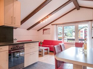 A kitchen with a stove, oven, and cabinets. There is a red sofa and a dining table with chairs. - Alouette Appartement/Fewo 6-Bettwohnung Nr. 18 by Interhome (Saas-Fee)