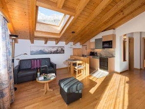 Ein modernes Interieur mit Holzbalkendecke, einem Essbereich, einer Küche und einem Wohnzimmer mit einer Couch und einem kleinen Tisch.