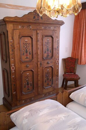 Um armário de madeira tradicional com desenhos florais detalhados, uma cadeira clássica e uma cama com colcha floral.