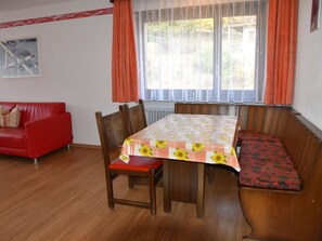 A dining area with a table covered in a floral tablecloth, wooden chairs, and a bench with a red cushion. - Acimo Appartement/Fewo 5-Bettwohnung Romeo & Julia by Interhome (Saas-Fee)