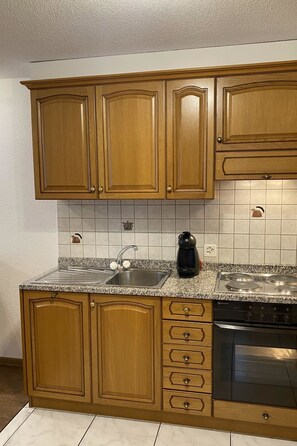 Una cocina con armarios de madera, encimera de granito, pileta, cafetera y estufa.