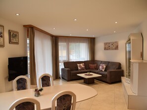Ein modernes Wohnzimmer mit einer Couch, einem Couchtisch, einem Esstisch, Stühlen und einem Fernseher.