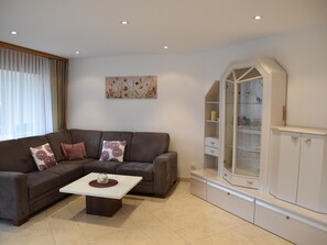Een woonkamer met een bruine modulaire bank, een witte salontafel en een kast met glazen deuren en lades.