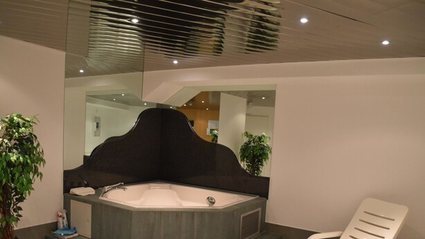 Een moderne badkamer met een vrijstaand bad, een grote spiegel en twee witte fauteuils.