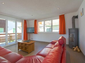 Una sala de estar con un sofá rojo, una mesa de centro de madera, un televisor y una estufa de leña.