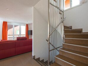 A staircase with metal railings leading to a landing, a red sofa, and a television in a room with a view of a wooden fence. - Chalet Les Arolles Appartement/Fewo 10-Bettwohnung by Interhome (Saas-Fee)