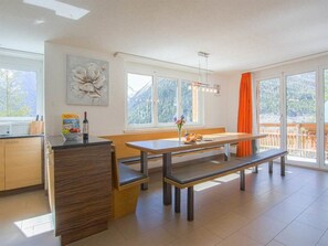 A modern kitchen with a wooden island, a dining table with benches, large windows with mountain views, and a bright interior. - Chalet Les Arolles Appartement/Fewo 10-Bettwohnung by Interhome (Saas-Fee)