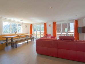A spacious living area with a red sofa, a wooden bench, and a dining table. - Chalet Les Arolles Appartement/Fewo 10-Bettwohnung by Interhome (Saas-Fee)