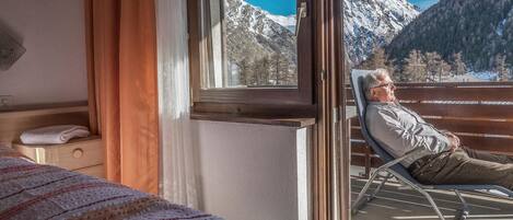 Una habitación con cama, ventana y vista a montañas nevadas, además de una silla junto a la ventana.