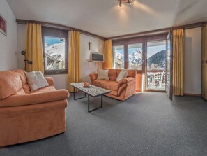 A living room with two sofas, a coffee table, and a TV on a wall. Large windows offer a mountain view. - Bergrose Appartement/Fewo 4-Bettwohnung Nr. 1 by Interhome (Saas-Fee)