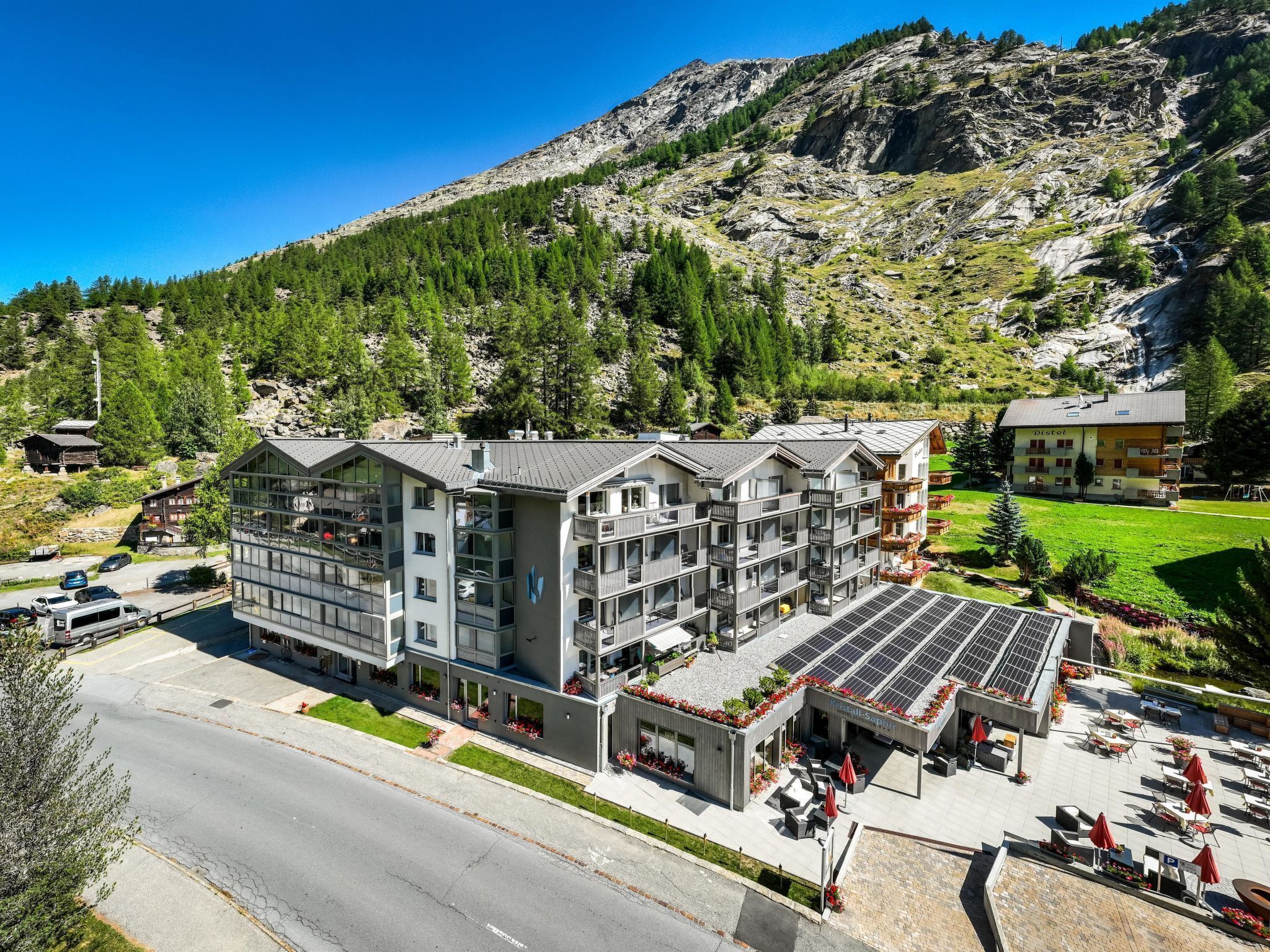 Un hotel de varios pisos con balcones, un jardín en la azotea y vistas a un paisaje montañoso.