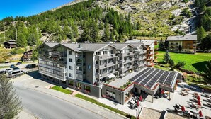 Um hotel com vários andares, varandas, um jardim no terraço e vista para uma paisagem montanhosa.