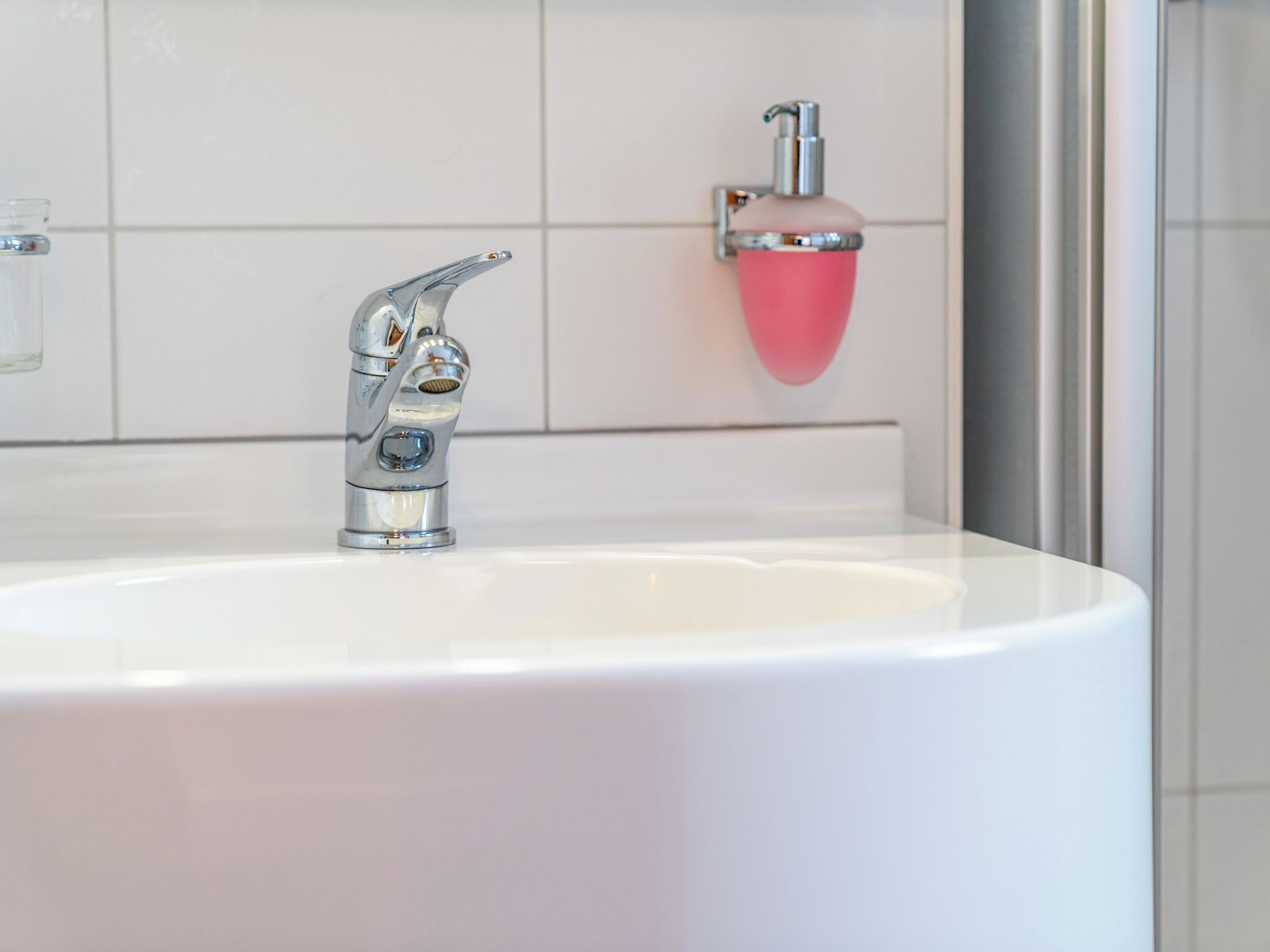 Et badeværelse med en hvid vask, en kromarmatur og en pink sæbedispenser.