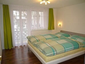 Een slaapkamer met een bed, gordijnen, een raam en een wandlamp.