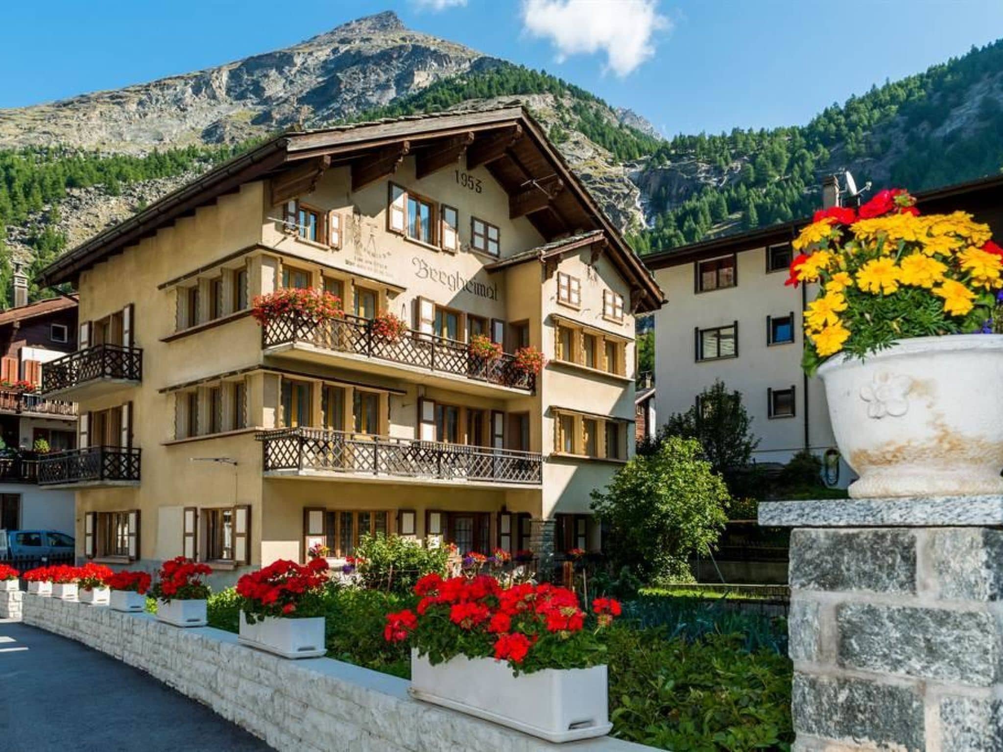 Ein mehrstöckiges Hotel mit Balkonen, einer Steinwand und einem Berg im Hintergrund.