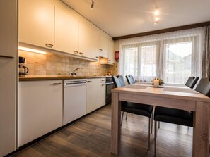 A modern kitchen with white cabinets, a dishwasher, a stove, and a dining area with a table and chairs. - Haus Adora Appartement/Fewo 4-Bettwohnung Nr. 4 by Interhome (Saas-Almagell)