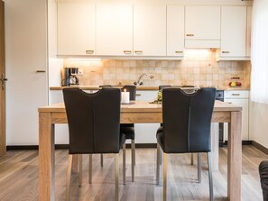 A modern kitchen with white cabinets, a wooden dining table, and two black chairs. - Haus Adora Appartement/Fewo 4-Bettwohnung Nr. 4 by Interhome (Saas-Almagell)