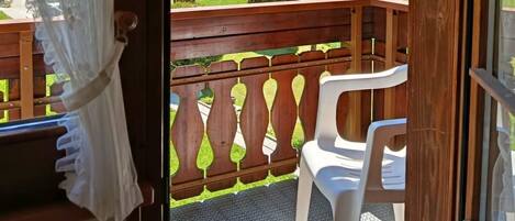 Ein Balkon mit Hollerkerbung, einem weißen Kunststoffstuhl und Blick auf eine Berglandschaft mit Gebäuden.